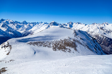 Obraz premium Caucasus Mountains, Panoramic view of the ski slope with the mountains Belalakaya, Sofrudzhu and Sulakhat on the horizon in winter day. Dombai ski resort, Western Caucasus, Karachai-Cherkess, Russia.