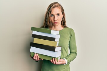 Young blonde woman holding a pile of books skeptic and nervous, frowning upset because of problem. negative person.