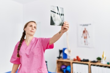Young caucasian woman wearing physiotherapist uniform holding xray at physiotherapy clinic