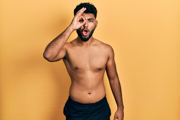 Fototapeta premium Arab man with beard wearing swimwear shirtless doing ok gesture shocked with surprised face, eye looking through fingers. unbelieving expression.