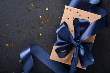 Holiday gift box or present with blue ribbon, golden confetti and gold baubles on black background....