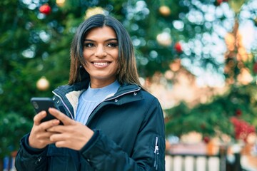 Young hispanic woman using smartphone outdoor by christmas decorations