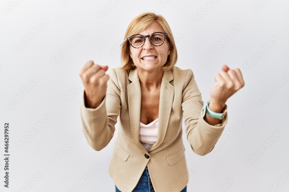 Sticker Middle age blonde business woman standing over isolated background angry and mad raising fists frustrated and furious while shouting with anger. rage and aggressive concept.