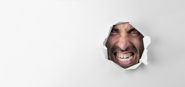 Angry insane man looking through the hole with red eyes on white background with copy space for advertising