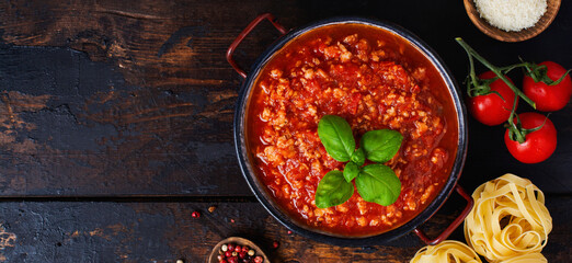 Traditional italian Bolognese sauce in saucepot an old dark wooden background. Top view, copy space