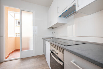 Kitchen with white and gray furniture and appliances with an exit door to the terrace inside the building