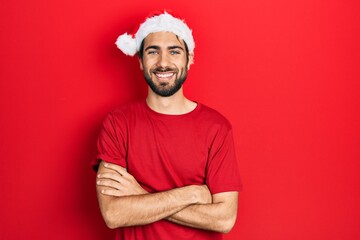 Young hispanic man wearing christmas hat happy face smiling with crossed arms looking at the camera. positive person.