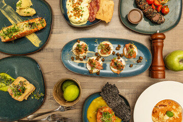 Set of international food dishes of fish, grilled salmon, Norwegian salmon blinis, red tuna tataki, hake in sauce, tartare, limes, forks and pepper