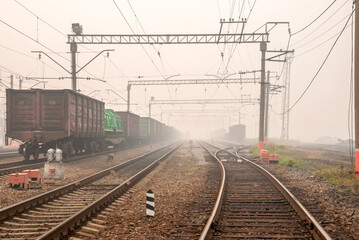 Freight terminal of railway trains. Railway tracks, cars and locomotive in fog.