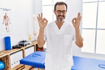 Middle age man with beard working at pain recovery clinic relax and smiling with eyes closed doing meditation gesture with fingers. yoga concept.