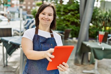 Young down syndrome woman wearing apron using touchpad at coffee shop terrace
