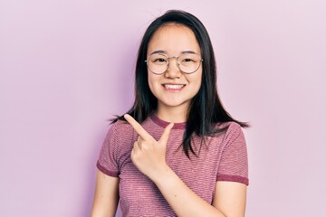 Fototapeta premium Young chinese girl wearing casual clothes and glasses cheerful with a smile of face pointing with hand and finger up to the side with happy and natural expression on face