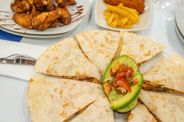 Mexican quesadillas stuffed with chicken tinga stew with ripe avocado, a tablespoon of pico de gallo and other dishes in the background