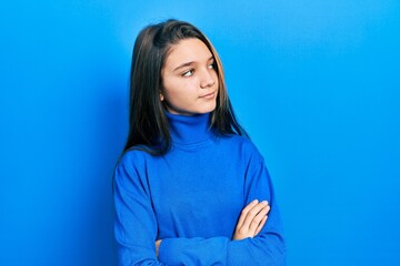 Young brunette girl wearing turtleneck sweater looking to the side with arms crossed convinced and confident