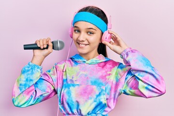 Young brunette girl singing song using microphone wearing sportswear smiling with a happy and cool smile on face. showing teeth.