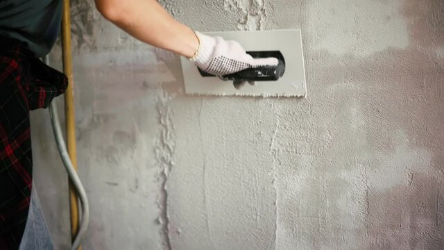 A close-up shot of a professional repairwoman puts a plaster on the wall with a spatula. Female repairing the wall with a putty knife.