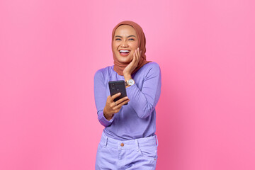 Portrait of smiling young Asian woman holding mobile phone on pink background