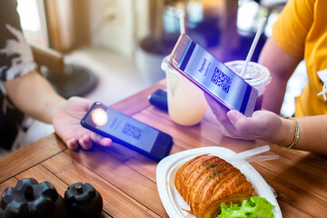 Customer hand using smart phone to scan QR code Tag on another smartphone with blur bread set meal in coffee shop or restaurant to accepted generate digital pay without money. Qr code payment concept.