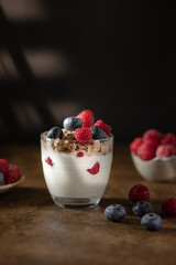 Bowl of granola with yogurt, milk and fresh raspberries, blueberries, mango for a healthy breakfast on the dark background