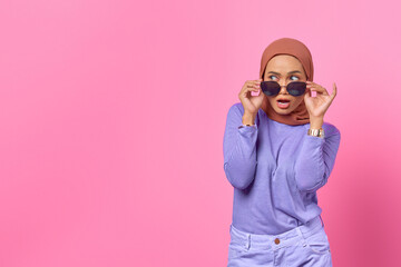 Portrait of shocked young Asian woman wearing glasses and looking aside on pink background