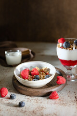 Bowl of granola with yogurt, milk and fresh raspberries, blueberries, mango for a healthy breakfast on the dark background
