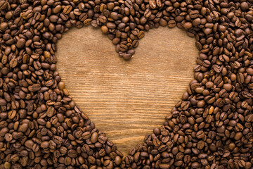 Heart shape created from fresh dark brown coffee beans. Empty place for text on wooden table background. Closeup. Top down view.
