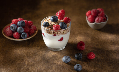 Bowl of granola with yogurt, milk and fresh raspberries, blueberries, mango for a healthy breakfast on the dark background