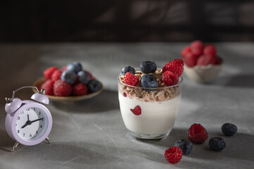 Bowl of granola with yogurt, milk and fresh raspberries, blueberries, mango for a healthy breakfast on the dark background