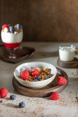 Bowl of granola with yogurt, milk and fresh raspberries, blueberries, mango for a healthy breakfast on the dark background