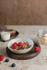 Bowl of granola with yogurt, milk and fresh raspberries, blueberries, mango for a healthy breakfast on the dark background