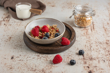 Bowl of granola with yogurt, milk and fresh raspberries, blueberries, mango for a healthy breakfast on the dark background