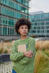 Pensive skilled female poet holds notepad and pen being deep in thoughts wears casual green sweater...