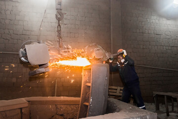 A male worker in a protective helmet, respirator, overalls manages heavy grinding equipment for...