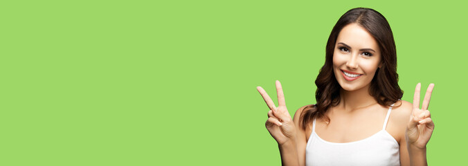 Photo of woman showing two fingers or victory hand sign gesture isolated on light green studio...