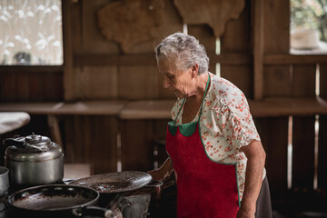 Retrato de una mujer adulta mayor cocinando en una estufa metálica con leña en su casa de madera 