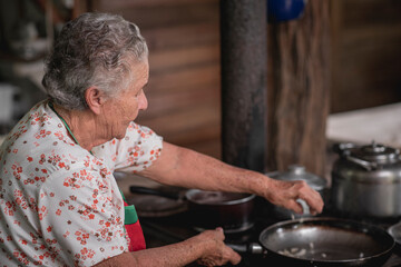 Retrato de una mujer adulta mayor cocinando en una estufa metálica con leña en su casa de madera 