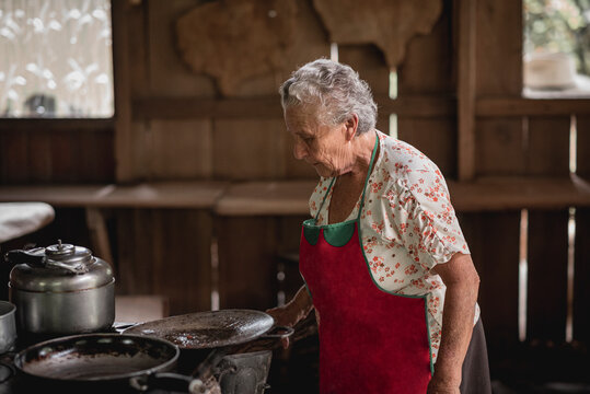 Retrato de una mujer adulta mayor cocinando en una estufa met&aacute;lica con le&ntilde;a en su casa de madera 