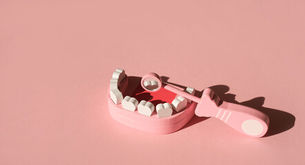 A model of a human jaw with a dental mirror reflecting a tooth on a pink studio background. Dental examination and prevention of dental diseases. Toy jaw and tool