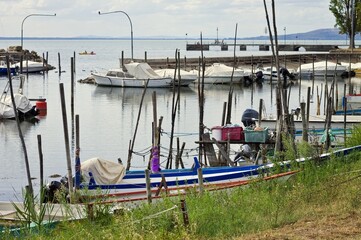 Small motor boats moored on wooden poles of the pier of a small port in Lake Trasimeno (Umbria, Italy, Europe) - 466309703