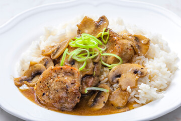 slices of pork meat with mushrooms and gravy served with rice