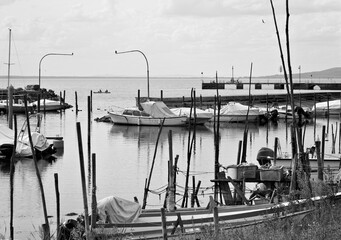 Small motor boats moored on wooden poles of the pier of a small port in Lake Trasimeno (Umbria, Italy, Europe) - 466309707