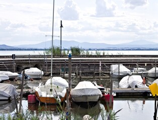 Small motor boats moored on wooden poles of the pier of a small port in Lake Trasimeno (Umbria, Italy, Europe) - 466309710