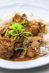 slices of pork meat with mushrooms and gravy served with rice