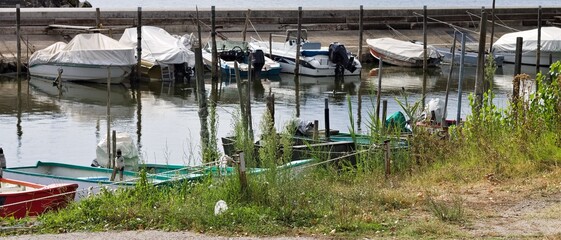 Small motor boats moored on wooden poles of the pier of a small port in Lake Trasimeno (Umbria, Italy, Europe) - 466309723