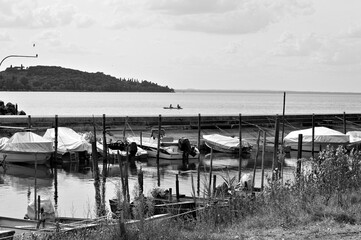 Small motor boats moored on wooden poles of the pier of a small port in Lake Trasimeno (Umbria, Italy, Europe) - 466309731