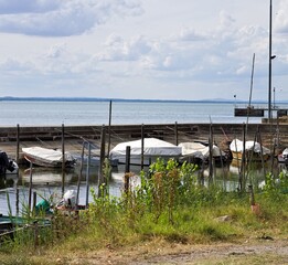Small motor boats moored on wooden poles of the pier of a small port in Lake Trasimeno (Umbria, Italy, Europe) - 466309736