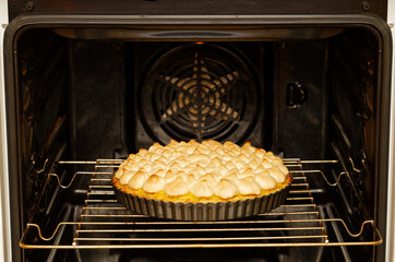 Closeup homemade pie decorated with meringue is prepared in the domestic oven.