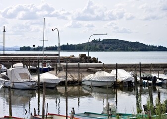 Small motor boats moored on wooden poles of the pier of a small port in Lake Trasimeno (Umbria, Italy, Europe) - 466309742