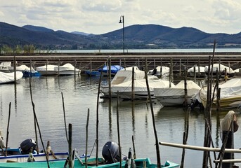 Small motor boats moored on wooden poles of the pier of a small port in Lake Trasimeno (Umbria, Italy, Europe) - 466309746