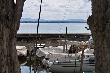 Small motor boats moored on wooden poles of the pier of a small port in Lake Trasimeno (Umbria, Italy, Europe) - 466309778